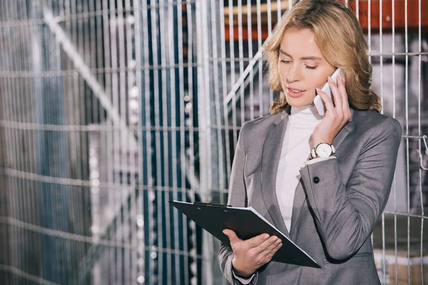 Attraente donna d'affari che parla su smartphone e tiene appunti in magazzino — Foto stock