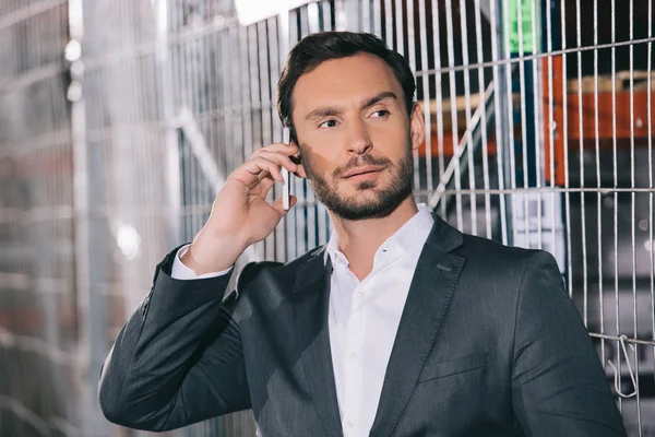 Confident businessman looking away while talking on smartphone in warehouse — Stock Photo