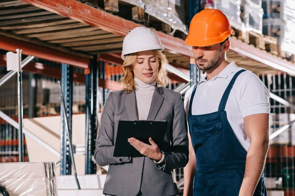 Concentrated businesswoman and warehouse worker looking at clipboard — Stock Photo