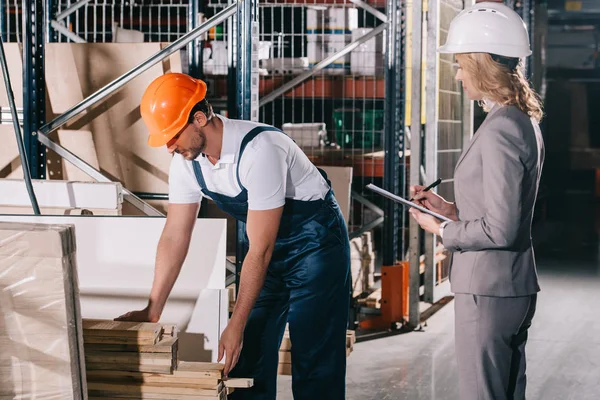 Businesswoman in helmet looking at loader standing near construction materials in warehouse — Stock Photo