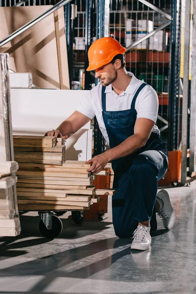 Lagerarbeiter steht auf Knien neben Gestell mit Holzplanken — Stockfoto