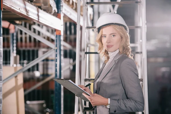 Confident businesswoman in helmet holding clipboard and looking at camera — Stock Photo