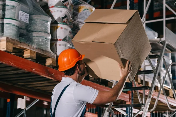 Trabalhador armazém segurando caixa de papelão enquanto em pé na escada rolante — Fotografia de Stock