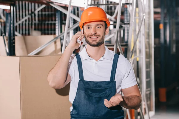 Lavoratore magazzino sorridente parlando su smartphone e mostrando gesto domanda — Foto stock