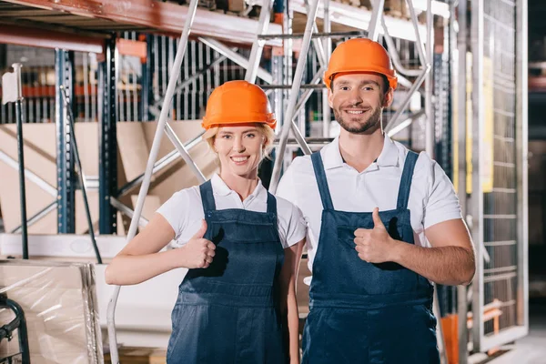 Cheerful warehouse workers showing thumbs up and smiling at camera — Stock Photo