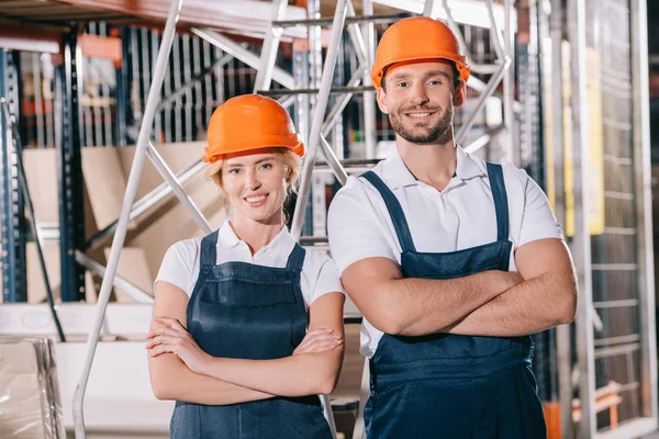 Cheerful warehouse workers standing with crossed arms and smiling at camera — Stock Photo