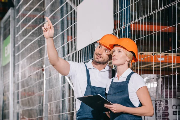 Arbeiterin hält Klemmbrett, während sie neben Arbeiter steht, wegschaut und mit Finger zeigt — Stockfoto