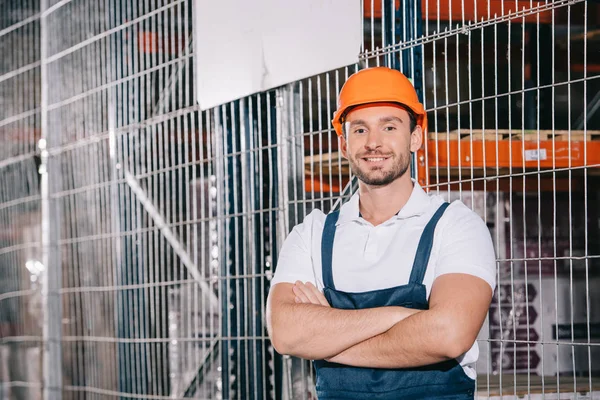 Gutaussehender Lader lächelt mit verschränkten Armen in die Kamera — Stockfoto