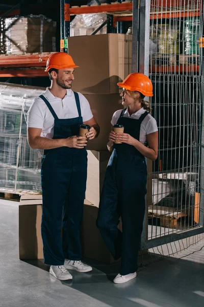 Smiling warehouse workers looking at each other while holding coffee to go — Stock Photo