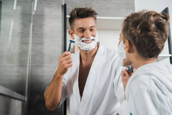 Selective focus of happy father with shaving foam on face looking at son in bathroom — Stock Photo