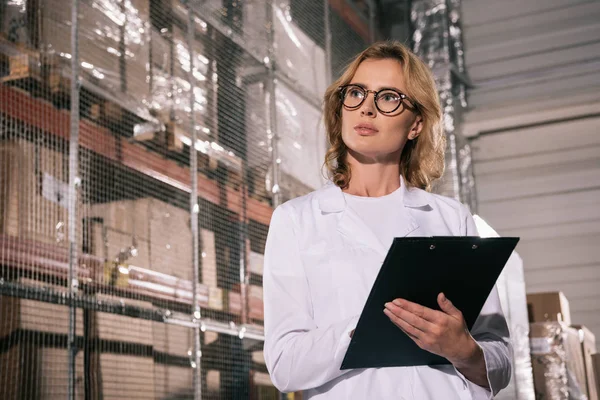 Attraktiver Ladenbesitzer in Brille, Klemmbrett in der Hand und wegguckend — Stockfoto