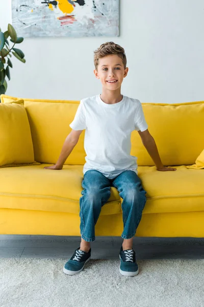 Happy boy in white t-shirt sitting on yellow sofa — Stock Photo