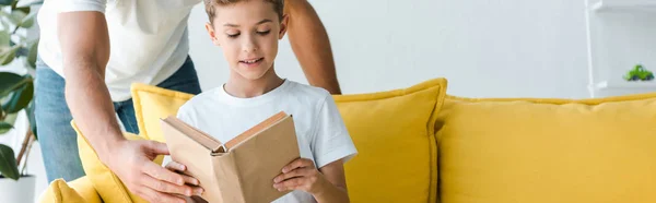 Panoramic shot of father standing near son with book — Stock Photo