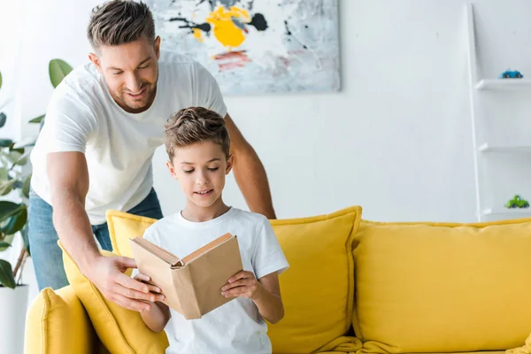 Feliz padre de pie cerca de hijo con libro - foto de stock