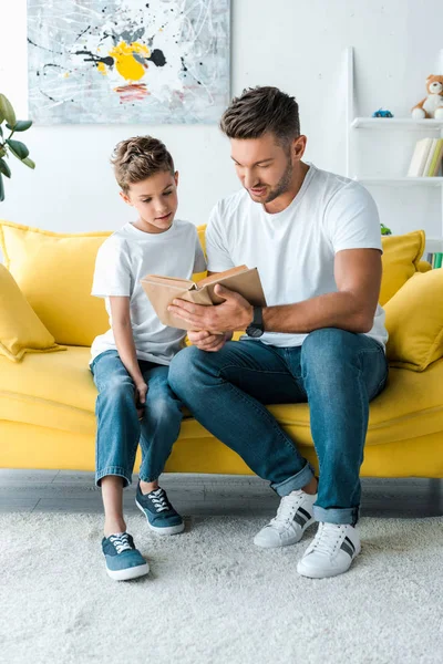 Beau père assis avec fils et livre de lecture — Photo de stock