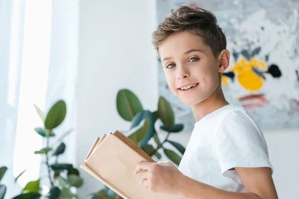 Feliz y lindo niño sosteniendo libro en casa - foto de stock