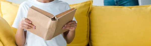 Plano panorámico de niño sosteniendo libro en casa - foto de stock