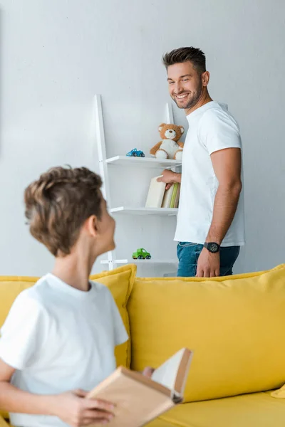 Вибірковий фокус веселого батька, який дивиться на сина з книгою — стокове фото