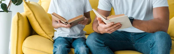 Tiro panorâmico de pai e filho segurando livros enquanto sentado no sofá — Fotografia de Stock