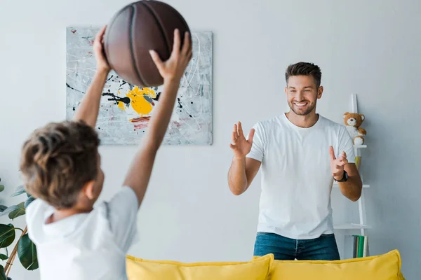 Избирательный фокус счастливого отца, смотрящего на сына с баскетболом — стоковое фото