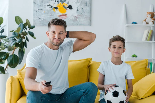 Guapo padre sosteniendo mando a distancia cerca de hijo con fútbol - foto de stock