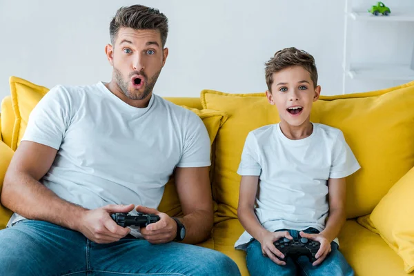 KYIV, UCRANIA - 2 de octubre de 2019: padre e hijo sorprendidos jugando videojuegos en casa - foto de stock