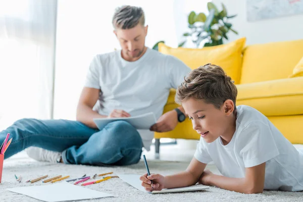 Messa a fuoco selettiva di bambino felice che disegna vicino a padre bello a casa — Foto stock