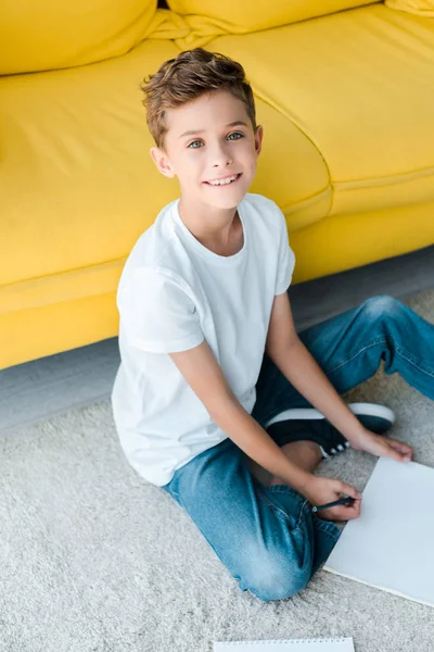 Happy kid sitting on carpet near yellow sofa at home — Stock Photo