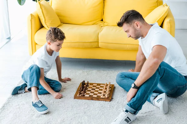 Bonito pai e bonito filho jogar xadrez no tapete em casa — Fotografia de Stock