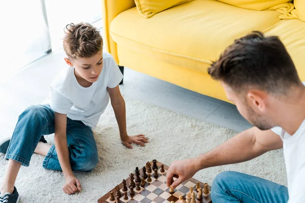 Overhead view of father and son playing chess on carpet — Stock Photo