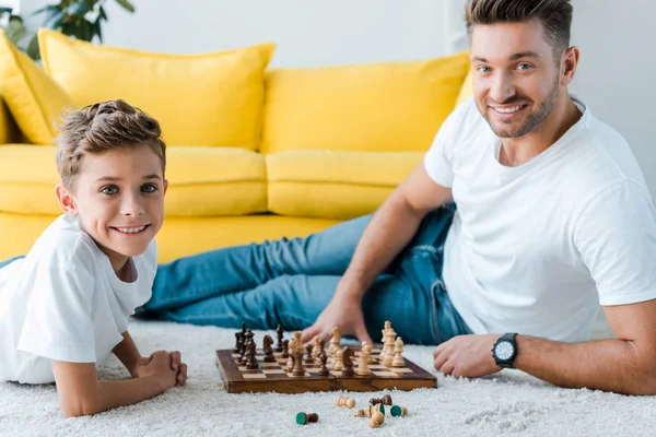 Feliz padre e hijo jugando ajedrez en la alfombra - foto de stock