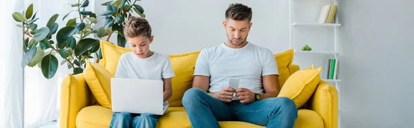 Tiro panorâmico de pai e filho usando gadgets em casa — Fotografia de Stock