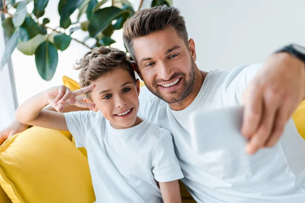 Foco seletivo de pai e filho felizes tomando selfie em casa — Fotografia de Stock