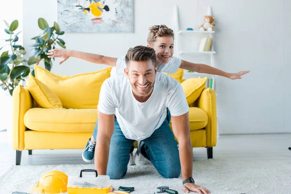 Enfant gai avec les mains tendues près du père heureux et boîte à outils jouet — Photo de stock