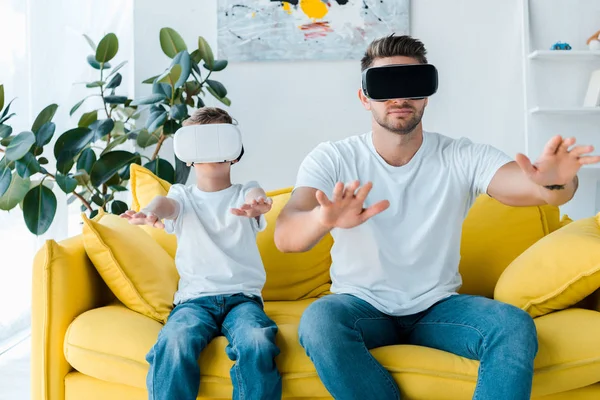 Padre e hijo en auriculares de realidad virtual haciendo gestos en la sala de estar - foto de stock