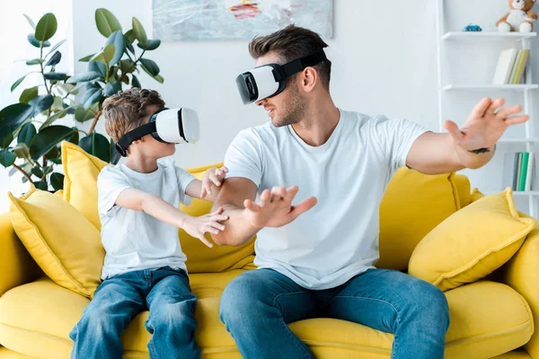 Happy father and son in virtual reality headsets gesturing in living room — Stock Photo