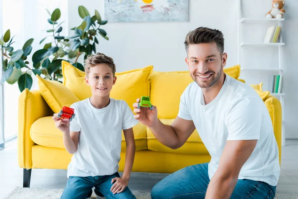 Счастливый сын и красивый отец играют с игрушечными машинами дома — стоковое фото
