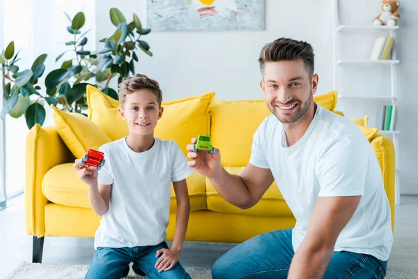 Feliz hijo y hermoso padre jugando con coches de juguete en casa - foto de stock