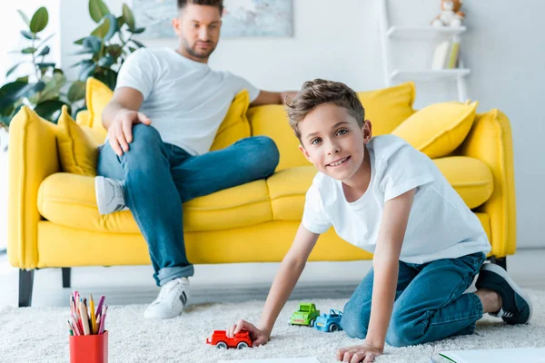 Selektiver Fokus des glücklichen Kindes, das mit Spielzeugauto in der Nähe des hübschen Vaters spielt — Stockfoto