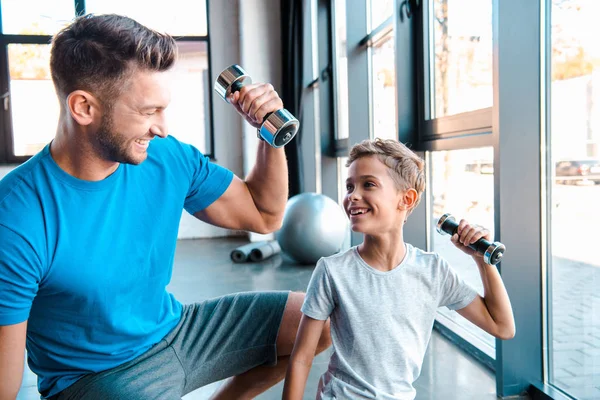 Handsome father looking at cheerful son while exercising with dumbbell — Stock Photo