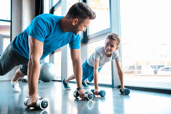 Happy father looking at cheerful son and exercising with dumbbells — Stock Photo