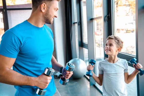 Happy father looking at cute son and exercising with dumbbells — Stock Photo