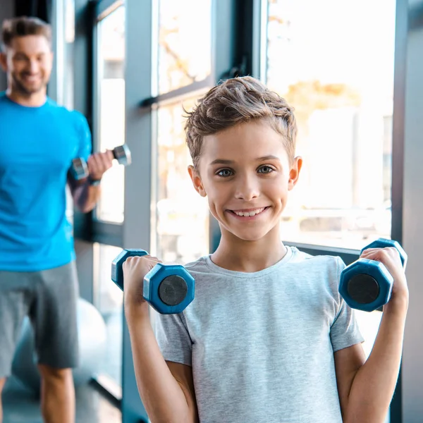 Selective focus cheerful kid exercising with dumbbells near father — Stock Photo