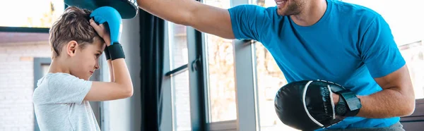 Panoramic shot of happy father and cute son boxing in gym — Stock Photo