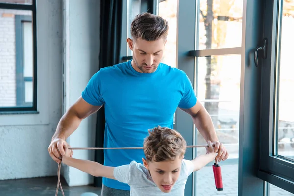 Enfoque selectivo de padre y niño guapo sosteniendo la cuerda de salto en el gimnasio - foto de stock