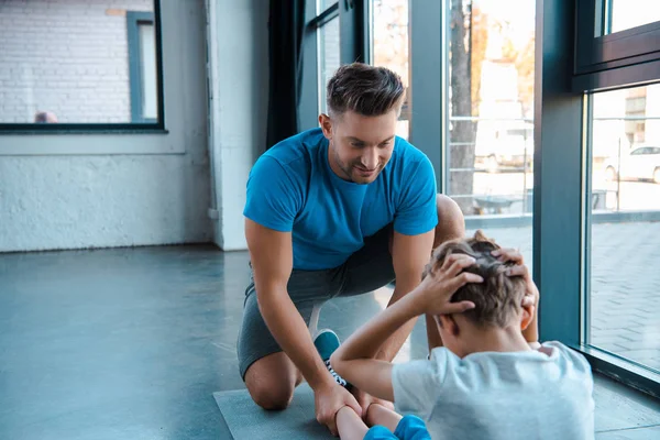 Enfoque selectivo de padre guapo mirando hijo haciendo abdominales en alfombra de fitness - foto de stock