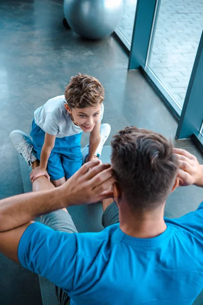 Blick von oben auf den niedlichen Sohn, der den Vater beim Training auf der Fitnessmatte beobachtet — Stockfoto