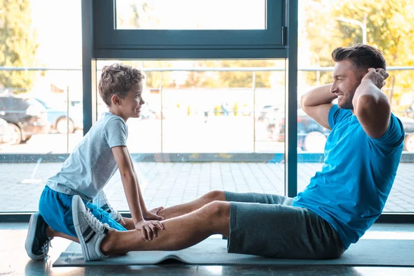 Seitenansicht des niedlichen Sohnes, der den Vater beim Training auf der Fitnessmatte beobachtet — Stockfoto