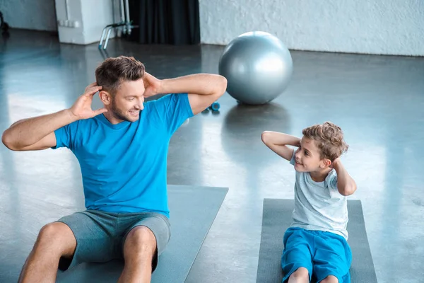 Niedliches Kind und Vater trainieren auf Fitnessmatten und schauen einander an — Stockfoto