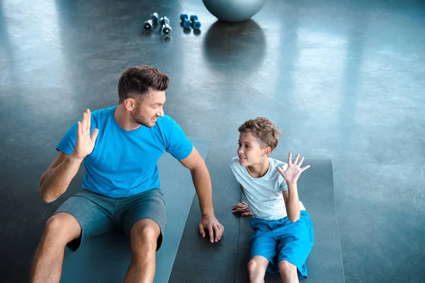 Cute kid and father looking at each other while giving high five in gym — Stock Photo